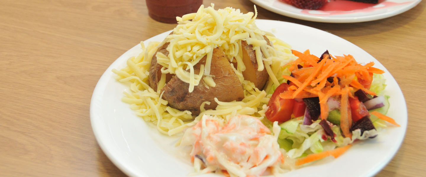 A white plate with a jacket potato with cheese, salad and coleslaw