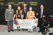A group pf five people smiling, Person 2 and 4 are holding a banner that says 'Barnsley College Construction Centre Garnd Opening, 11 March 2016. The person on the right has a pair of scissors in their right hand and a black dog in their left hand.