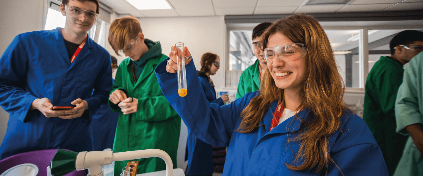 student smiling holding test tube surrounded by other students in lab coats