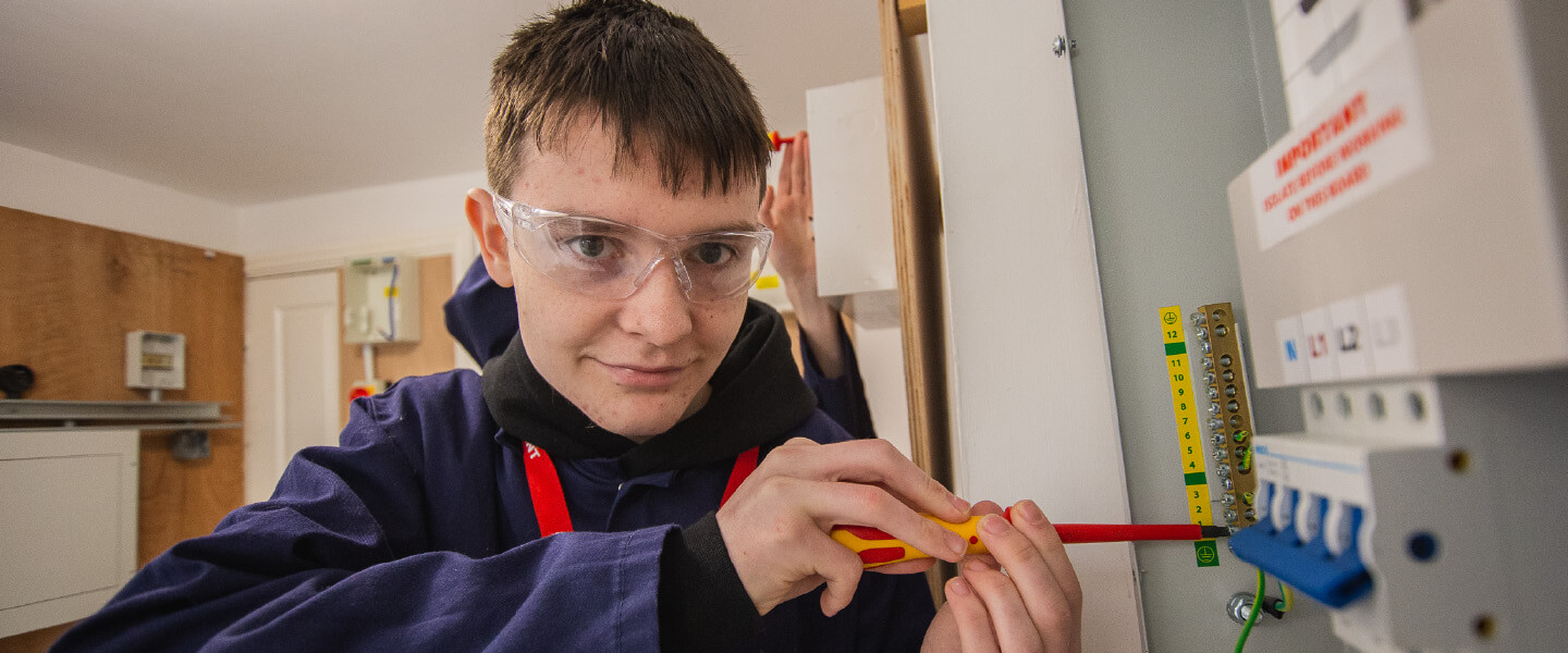 student smiling in googles holding screw driver