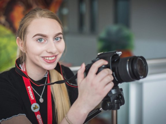 A Barnsley College student holding a camera and smiling.