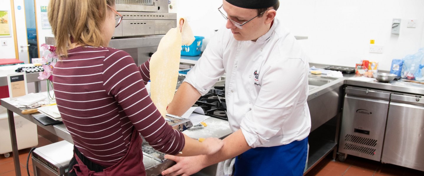General image of two catering students in kitchen cooking