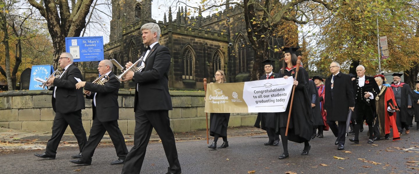 A photo of the start of the Graduation procession featuring some of the brass band, the banner, and the start of the procession featuring the mayor.