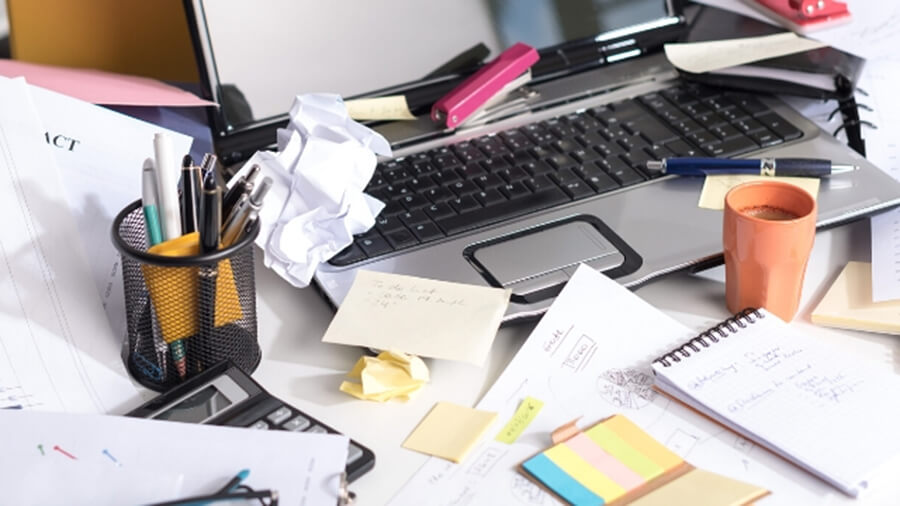 Stock image of messy desk, laptop covered in pens and bits of paper