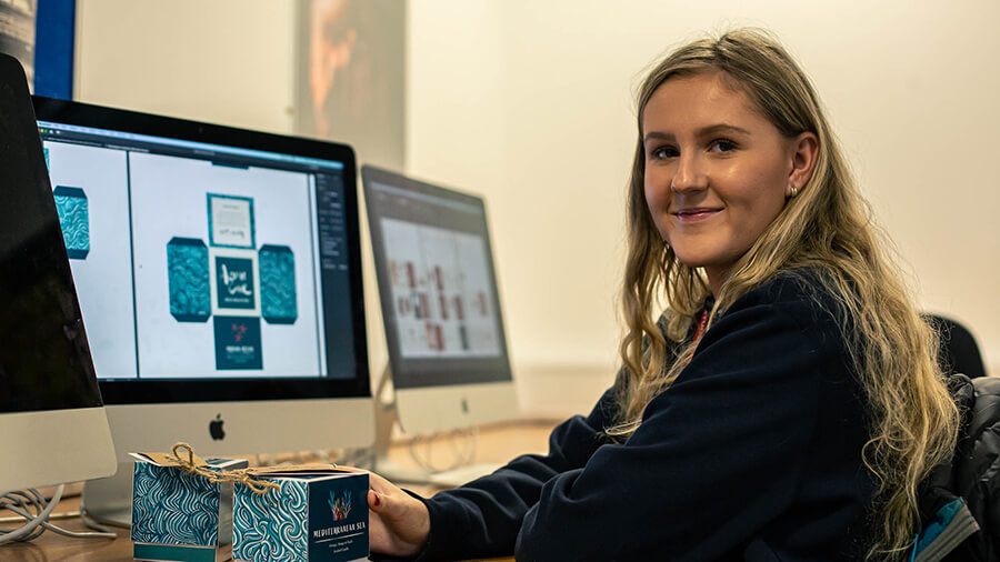 Female student sat at computer desk smiling at camera