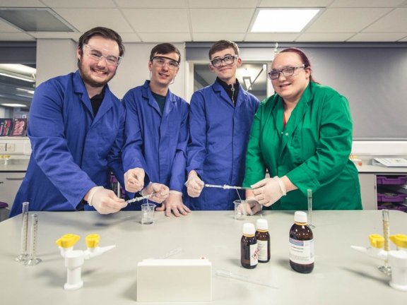 Barnsley College students smiling at the camera in a science lab.