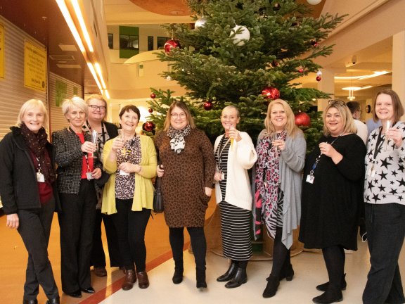 College staff in front of Christmas Tree raising a glass of prosecco.