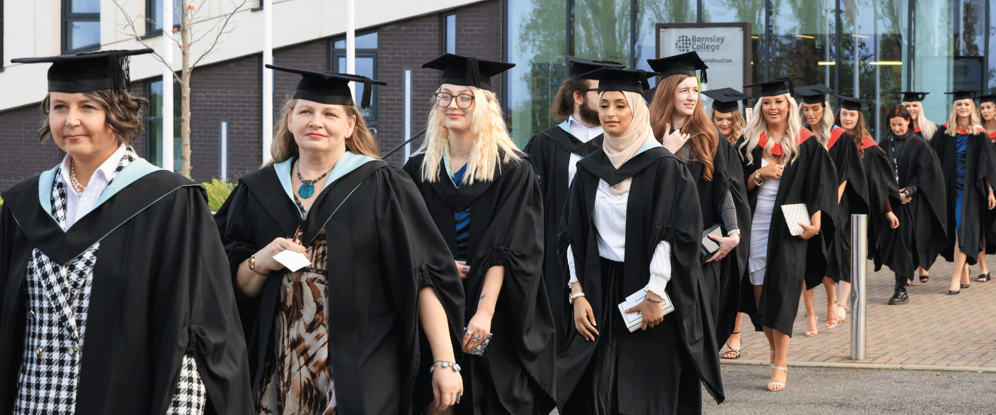 A line of graduates walk dressed in their robes and ceremonial caps