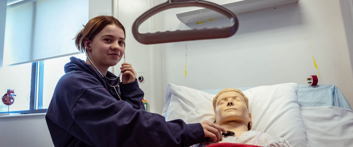 student smiling with stethoscope on first aid dummy