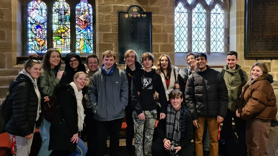 A photo of Barnsley College Performing Arts students in Eyam Church beneath the stained glass window dedicated to the Plague story.