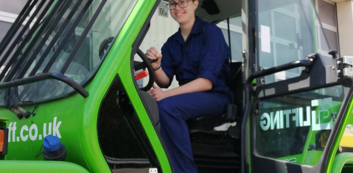 Isabelle Goddard, dressed in blue overalls, sitting in a green tractor