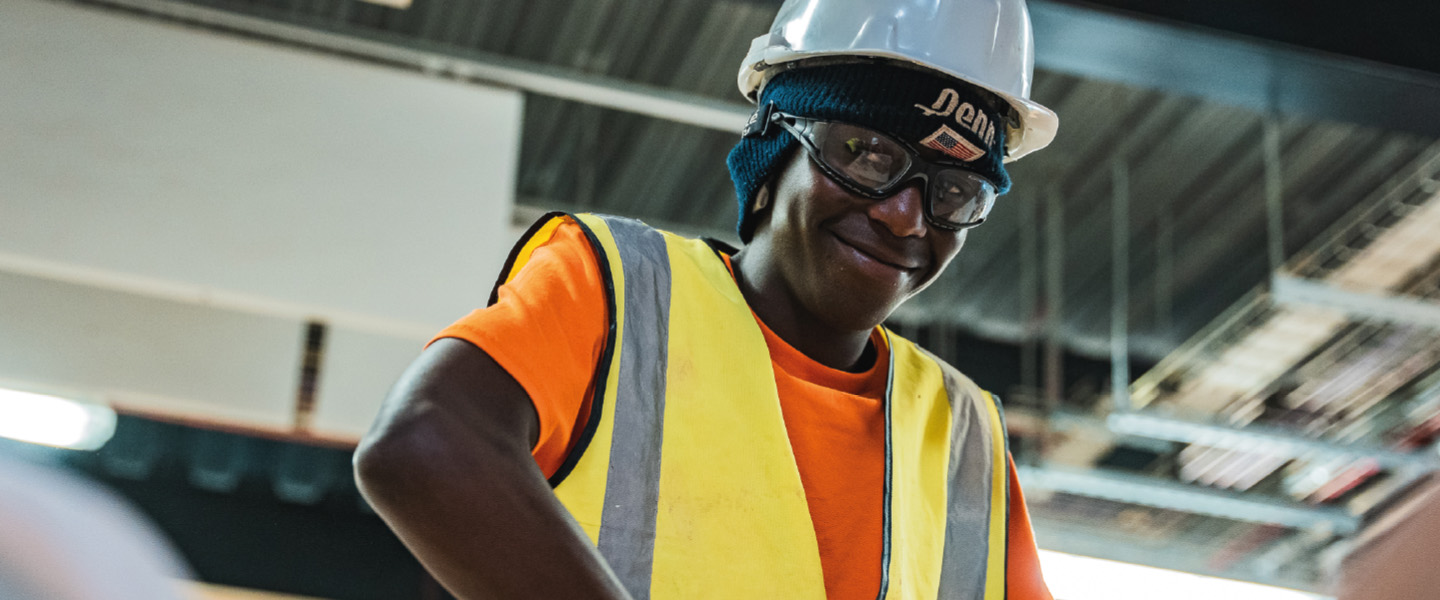 Boy wearing safety goggles and hardhat smiles at the camera