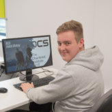 Harrison Baxter smiling with hands on keyboard and sat at computer