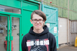 Image of a student in a black hoody stood smiling outside of a green barn