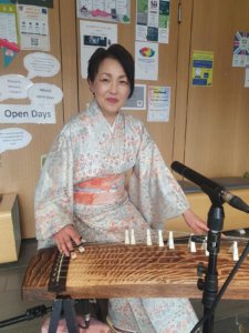 Person in traditional Japanese dress with a Koto (a traditional Japanese musical instrument)