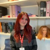 Amy Webster smiling into the camera, with red hair and a grey stripy jumper.