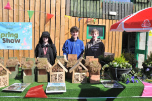 three students stood behind a table with homemade bee houses, bird boxes and hanging flower baskets