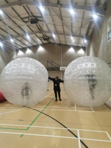 two students in zorbing balls with a trainer holding them