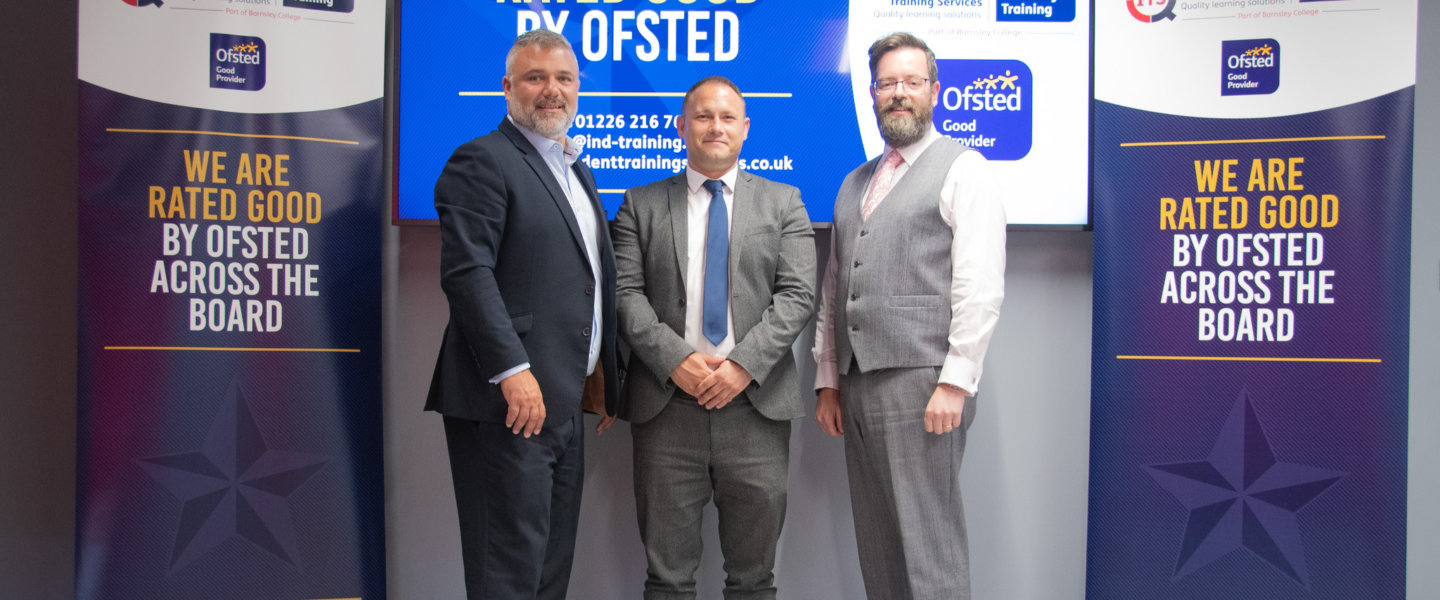 Three people stood in front of a tv screen with two banners stating ITS have achieved good across the board when judged by OFSTED.