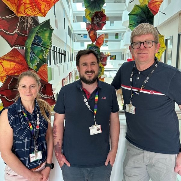 Barnsley College staff Abby Parkin, Gavin Mitchell and Rob Lea stood together inside the Old Mill Lane campus in front of decorative umbrellas.
