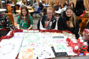 Three students selling animal prints at the Christmas Fair created by the animals at the farm