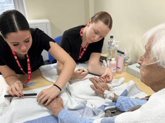 Two BC beauty students conducting a manicure on a hospital patient.