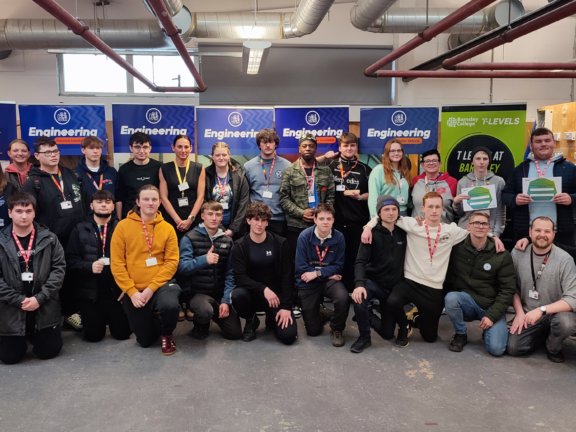 A large group of Barnsley College Engineering students, some holding awards, stand in a classroom at the RAEng competition.