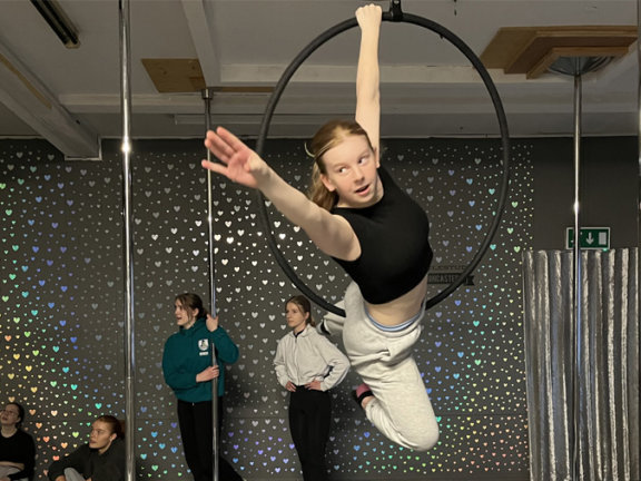 Student performing a dance move whilst hanging on a hoop.